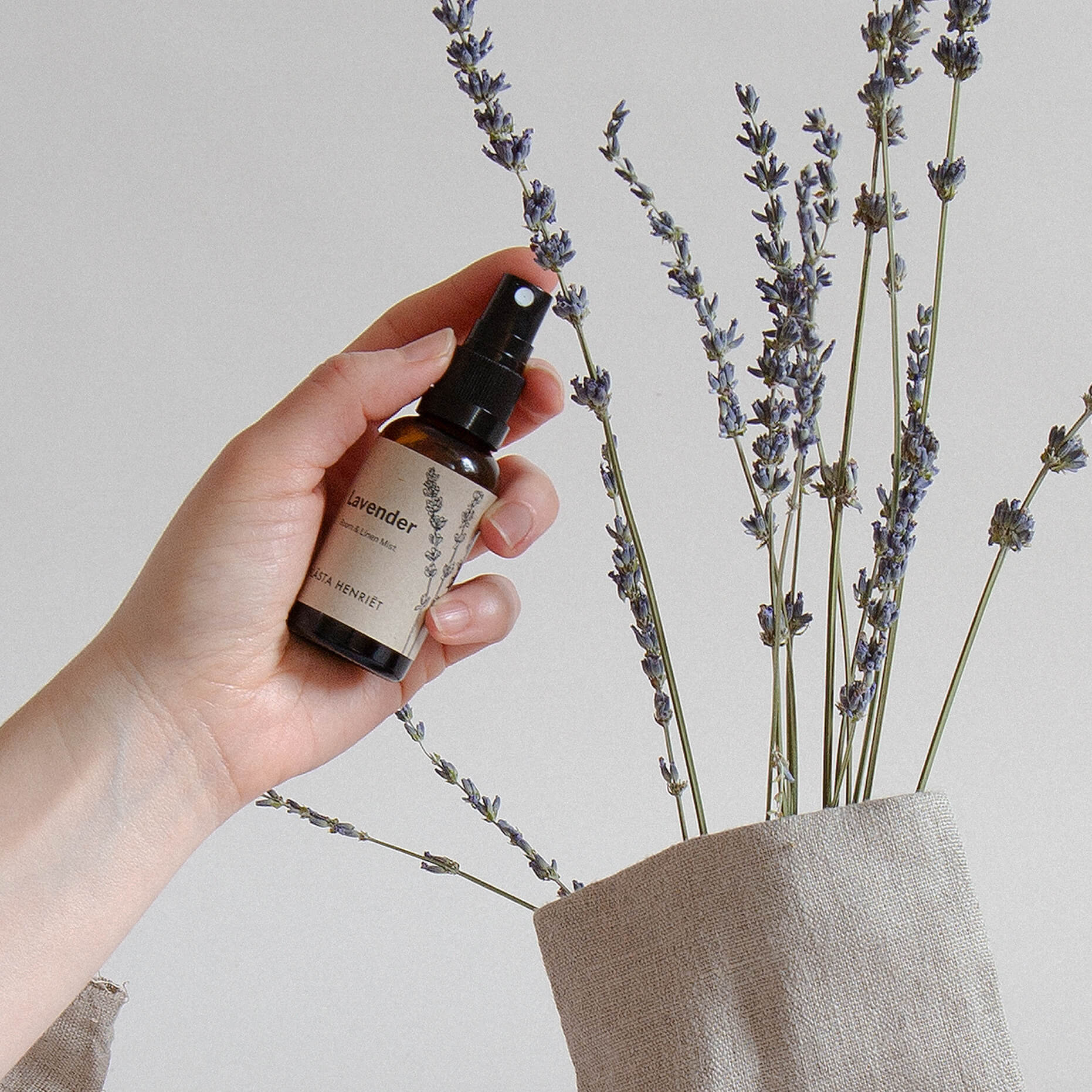 lavender room mist in brown glass bottle held by hand to a backdrop of natural lavender sprigs